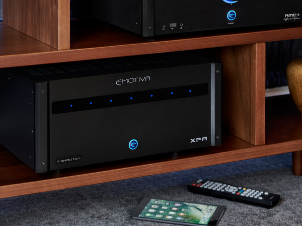 Emotiva XPA audio component on a wooden shelf with remote control and smartphone.